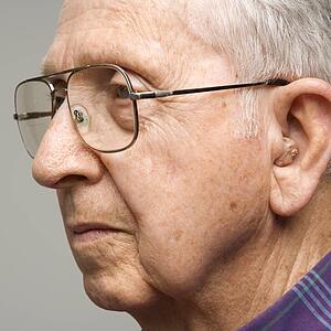 Close-up profile portrait of elderly man with glasses and hearing aid.