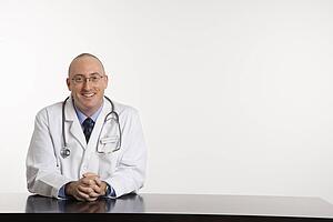 Caucasian mid adult male physician sitting at desk smiling.