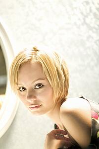 Portrait of attractive young adult blond woman making eye contact with fabric off bare shoulder.