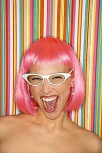 Portrait of attractive young adult woman wearing pink wig against striped background making sassy expression looking at viewer