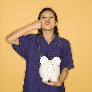 A mid-adult woman doctor holding piggy bank against yellow background and touching nose.