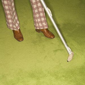 Close-up of Caucasian male feet with vacuum extension against green retro carpet.