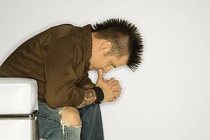 man with mohawk sitting with hands to face 