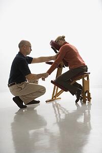Male massage therapist massaging arms and hands of woman sitting in massage chair