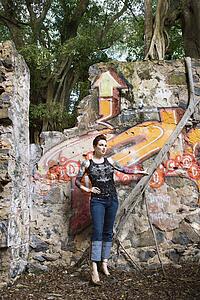 Sexy tattooed Caucasian woman standing next to wall covered in graffiti and a tree branch.