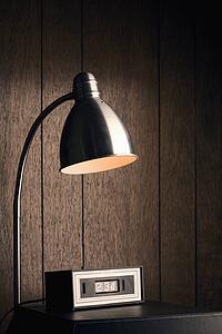 Desk lamp shining down on retro clock against wood paneling