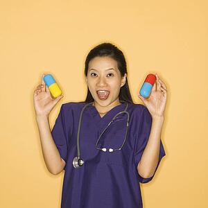 Asian Chinese mid-adult female doctor holding up giant pills against yellow background smiling and looking at viewer.