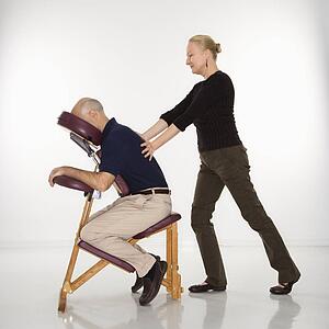 Massage therapist massaging back of man sitting in massage chair
