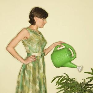 Pretty Caucasian mid-adult woman wearing vintage dress watering houseplant with green watering can.