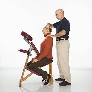 Massage therapist massaging neck of woman sitting in massage chair