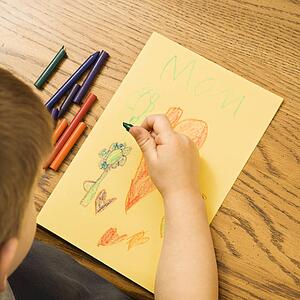 Caucasian boy drawing on paper with crayons.