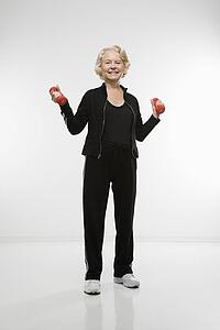 Caucasian senior woman holding dumbbells smiling at viewer.