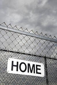 Home sign hanging on metal chain link fence.