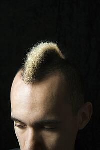 Portrait of Caucasian man in suit with mohawk against black background.