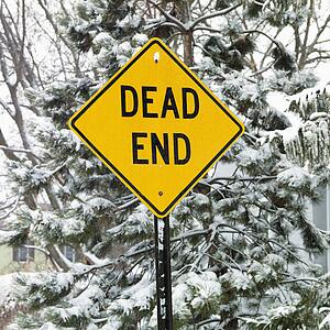Snowy scene in suburb with evergreen trees and dead end road sign.