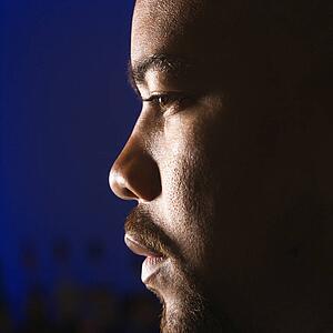 Close up profile of African American man in bar against glowing blue background.