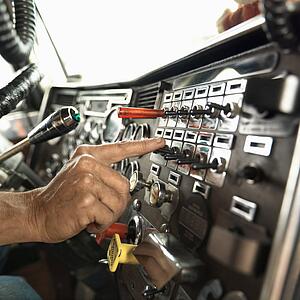 Interior of mid-adult Caucasian male hand pressing switch on dashboard of a tractor trailer.