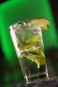 Cocktail with mint leaves and fruit garnish against glowing green background