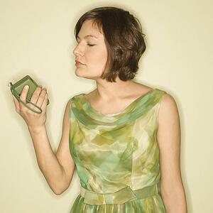 Pretty Caucasian mid-adult woman wearing green vintage dress looking at handheld radio.