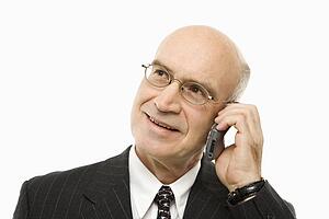 Caucasian middle-aged businessman talking on cellphone smiling against white background.