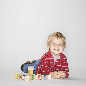 Studio portrait of young boy laying on stomach propped up on elbows playing with toy blocks