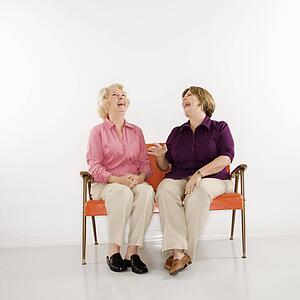 Middle aged woman and senior woman sitting and laughing