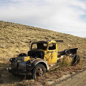 Old yellow dilapidated pickup truck sitting abandoned on hill