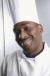 Head shot of chef wearing traditional uniform and toque looking at viewer smiling