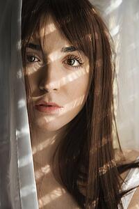 Portrait of pretty Caucasian young woman standing in sunlit curtains.