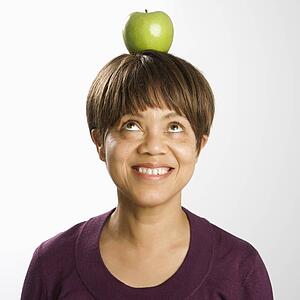 Portrait of middle-aged woman balancing green apple on head looking up and smiling
