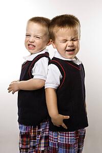 Caucasian twin boys crying standing against white background.