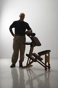 Silhouette of middle-aged male massage therapist standing with elbow on massage chair