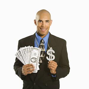 African American man in suit wearing necklace with money sign and holding cash.