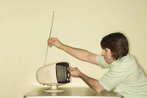 Man sitting at 50's retro dinette set adjusting old television antenna