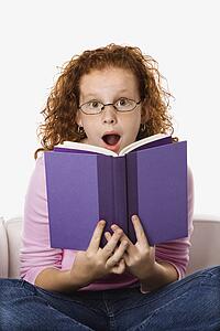Caucasian female child sitting reading book looking surprised.