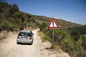 Car heading down dirt road with caution sign.
