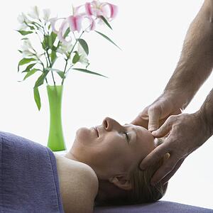 Middle-aged male massage therapist massaging temples of middle-aged woman laying on massage table