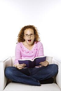 Caucasian female child sitting reading book looking surprised.