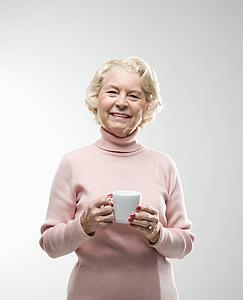 Caucasian senior woman holding coffee cup smiling at viewer.
