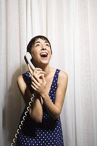 Woman holding telephone receiver to ear and laughing