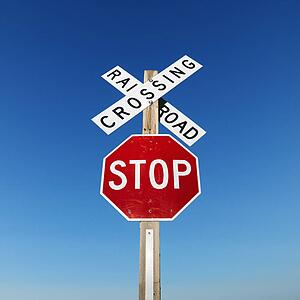 Railroad crossing and stop signs against blue sky.