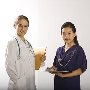 Caucasian mid-adult female doctor and Asian Chinese mid-adult female physician's assistant standing together smiling and looking at viewer.