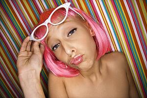 Woman wearing pink wig against striped background making sassy expression