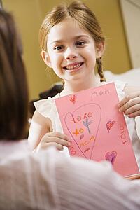 Caucasian girl giving mid adult mother a drawing.