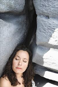 Portrait of brunette Caucasian mid-adult woman by rock formation with eyes closed.