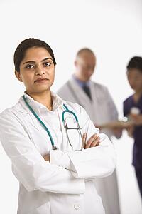 Indian mid adult woman doctor standing with medical staff in background.