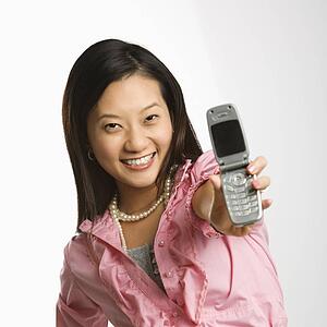 Portrait of Asian Chinese mid-adult female smiling and holding out cell phone towards viewer.