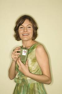 Pretty Caucasian mid-adult woman wearing green vintage dress holding up handheld radio for viewer to see.