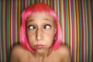 Portrait of attractive young adult woman wearing pink wig against striped background making cross eyed expression.