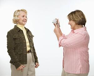 Middle aged woman taking photo of senior woman with digital camera.